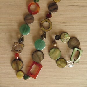 May include: A multi-colored necklace with round and square shaped beads in shades of brown, green, orange, and gold. The necklace is made of glass and metal.