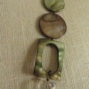 May include: A necklace with a variety of green and brown shell beads, including a square bead with a hole in the center, and a clear crystal bead.