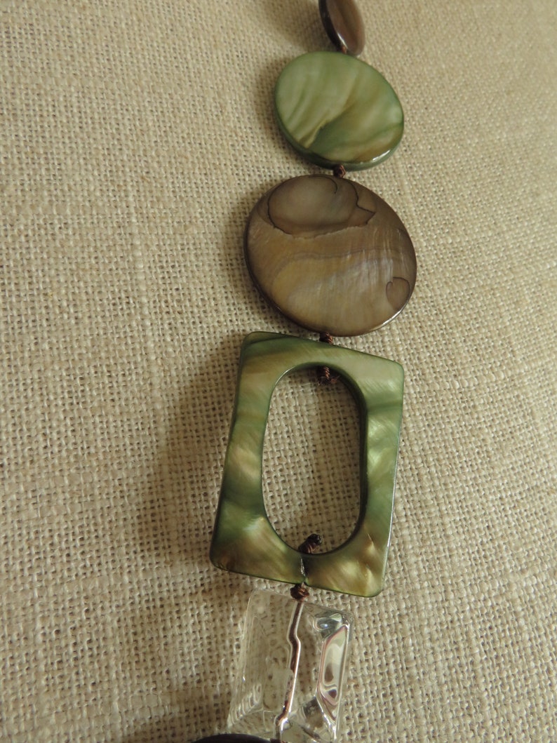 May include: A necklace with a variety of green and brown shell beads, including a square bead with a hole in the center, and a clear crystal bead.