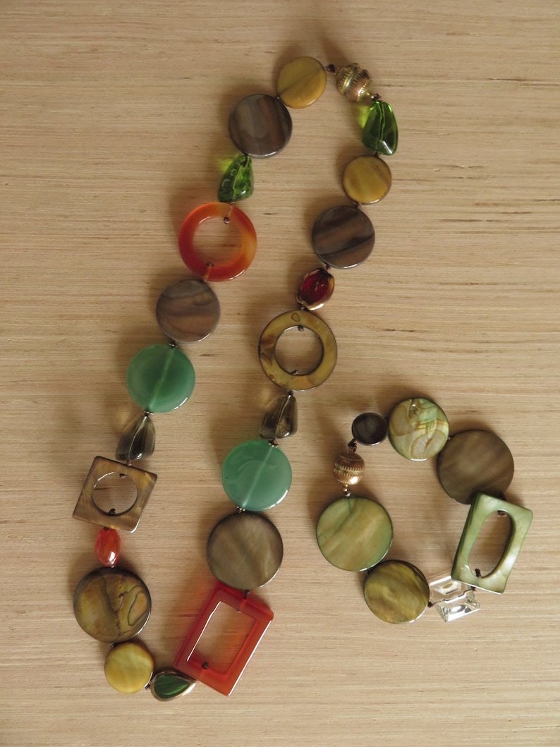 May include: A multi-colored necklace with round and square shaped beads in shades of brown, green, orange, and gold. The necklace is made of glass and metal.