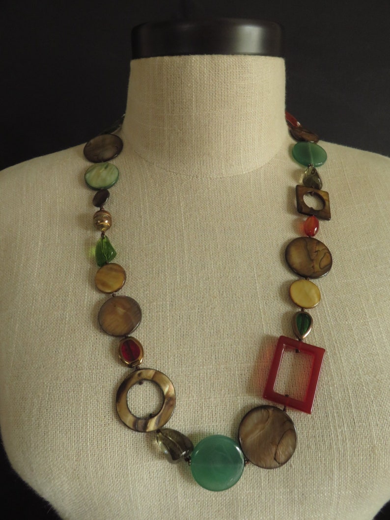 May include: A long necklace made of brown, green, and red beads. The beads are various shapes, including circles and squares.
