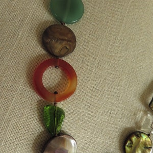 May include: A multi-colored necklace with round, flat beads. The beads are made of different materials, including green, brown, orange, and iridescent.