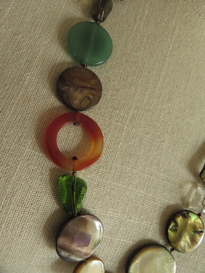 May include: A multi-colored necklace with round, flat beads. The beads are made of different materials, including green, brown, orange, and iridescent.
