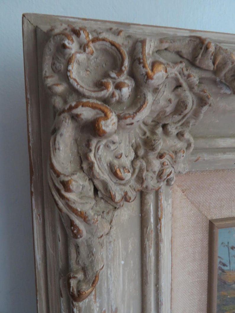 Puede incluir: Primer plano de una esquina de un marco de fotos vintage. El marco est&aacute; pintado en un color blanquecino desgastado con detalles dorados. Las tallas y detalles ornamentados son visibles, mostrando una est&eacute;tica cl&aacute;sica y antigua.