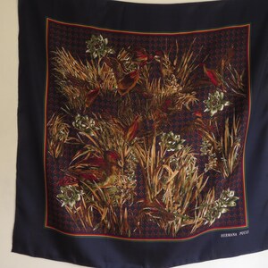 Puede incluir: Un pa&ntilde;uelo cuadrado de seda con un borde azul marino y un dise&ntilde;o central con p&aacute;jaros, plantas y flores en tonos marrones, verdes y rojos. El pa&ntilde;uelo tiene un fondo estampado y el texto "HERMANA PUCCI" en la esquina inferior derecha.