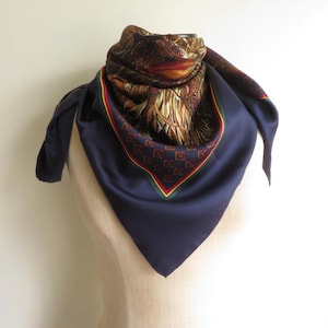 Puede incluir: Un pa&ntilde;uelo de seda azul marino con un dise&ntilde;o detallado de cabeza de p&aacute;jaro y plumas en tonos marr&oacute;n, rojo y dorado. El pa&ntilde;uelo cuadrado tiene un borde estampado en rojo, verde y dorado.