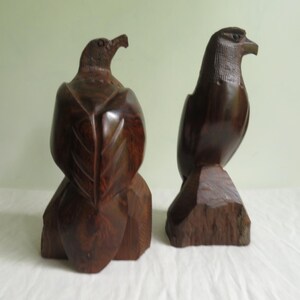 May include: Two dark brown wooden eagle sculptures. The eagles are carved in a realistic style and are perched on wooden bases.