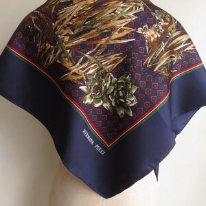 Puede incluir: Un pa&ntilde;uelo cuadrado de seda con borde azul marino y un estampado floral y bot&aacute;nico en tonos marr&oacute;n, verde y beige. El pa&ntilde;uelo tiene un ribete rojo y amarillo y el texto "HERMANA PUCCI" en blanco.