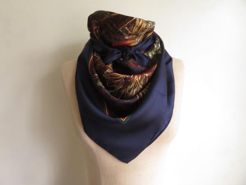 Puede incluir: Un pa&ntilde;uelo de seda azul marino con un dise&ntilde;o detallado y estampado en tonos marrones, verdes y rojos. El pa&ntilde;uelo est&aacute; drapeado alrededor de un maniqu&iacute;, mostrando su forma y textura. El pa&ntilde;uelo est&aacute; anudado al cuello.