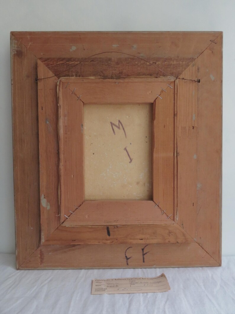 Puede incluir: Parte trasera de una obra de arte enmarcada con un marco de madera marr&oacute;n claro. La obra de arte est&aacute; asegurada con grapas. La parte trasera de la obra de arte tiene las letras "M" e "I" escritas con un rotulador azul. El marco tiene las letras "FF" escritas con rotulador negro.
