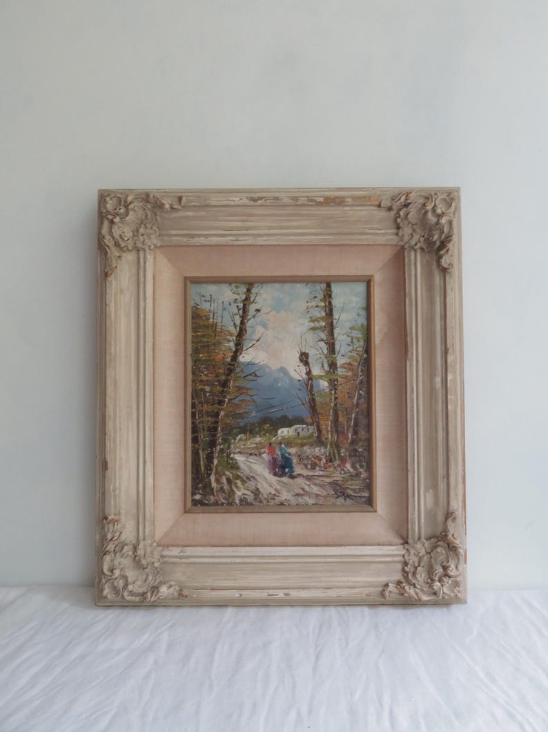 Puede incluir: Pintura al &oacute;leo enmarcada antigua que representa un paisaje de monta&ntilde;a con un camino y figuras. El marco es ornamentado, con un acabado blanquecino envejecido. La pintura presenta una paleta de colores apagados con azules, verdes y marrones.