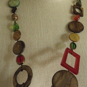 May include: A long necklace with brown, beige, and green round beads, and red and brown square beads.