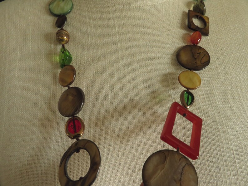 May include: A long necklace with brown, beige, and green round beads, and red and brown square beads.