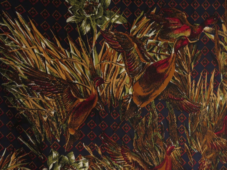 Puede incluir: Una tela con un patr&oacute;n repetido de patos en vuelo entre juncos y follaje. Los patos est&aacute;n representados en tonos marrones, naranjas y rojos, con las alas extendidas. El fondo es azul oscuro con un patr&oacute;n de diamantes.