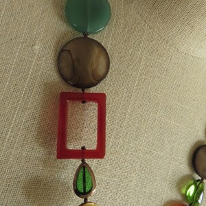 May include: A multi-colored necklace with round, oval, and rectangular beads. The beads are made of various materials, including glass, wood, and metal. The necklace is strung on a brown cord.