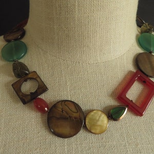 May include: A multi-colored necklace with round and square shaped beads. The beads are made of wood, stone, and glass. The necklace is brown, green, red, and white.