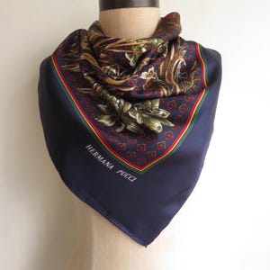 Puede incluir: Un pa&ntilde;uelo de seda azul marino con un estampado floral y geom&eacute;trico. El pa&ntilde;uelo tiene un borde rojo, verde y amarillo y el texto "HERMANA PUCCI" est&aacute; impreso en la esquina. El pa&ntilde;uelo est&aacute; drapeado sobre un maniqu&iacute;.