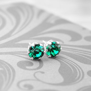 May include: A pair of silver stud earrings with emerald green gemstones.