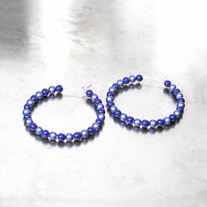 May include: A pair of hoop earrings made of iridescent blue beads. The earrings are silver and have a simple design.