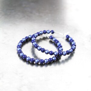 May include: A pair of hoop earrings made of blue iridescent beads. The earrings are silver toned and have a simple design.