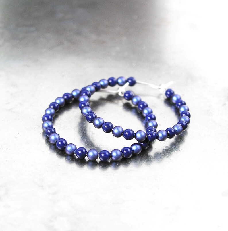 May include: A pair of hoop earrings made of blue iridescent beads. The earrings are silver toned and have a simple design.