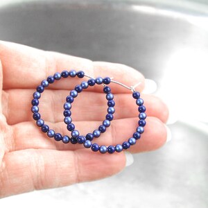 May include: A pair of hoop earrings made of silver wire and blue beads. The beads are small and round, and they are evenly spaced around the hoop.