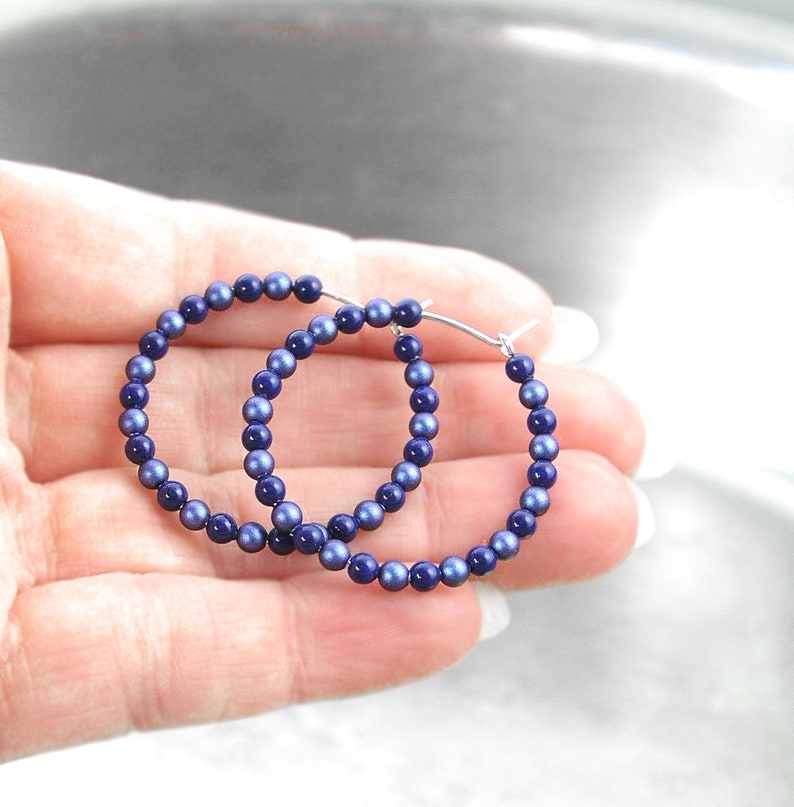 May include: A pair of hoop earrings made of silver wire and blue beads. The beads are small and round, and they are evenly spaced around the hoop.