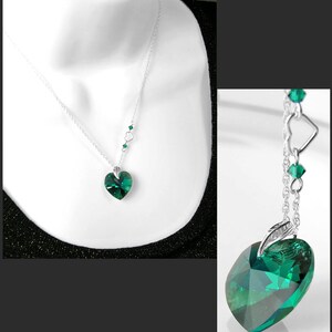 May include: A silver chain necklace with a large emerald green heart-shaped crystal pendant. The chain has smaller emerald green crystals and silver heart charms.