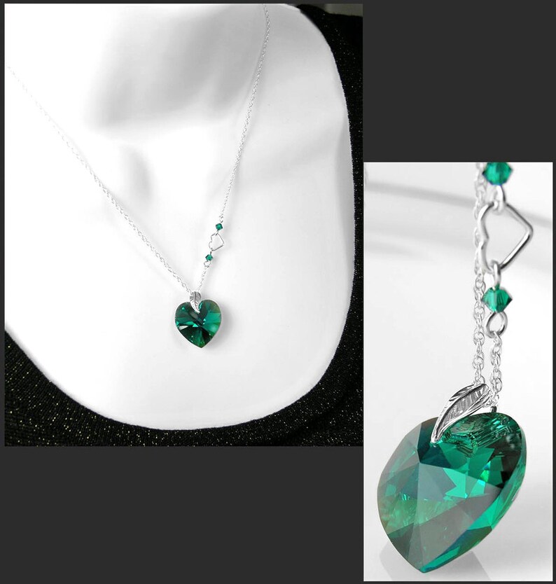 May include: A silver chain necklace with a large emerald green heart-shaped crystal pendant. The chain has smaller emerald green crystals and silver heart charms.