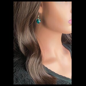 May include: A pair of dangle earrings with a heart-shaped emerald green crystal pendant.