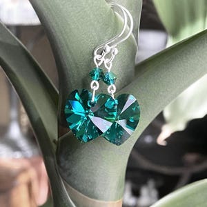 May include: A pair of silver dangle earrings with emerald green heart-shaped crystal accents.