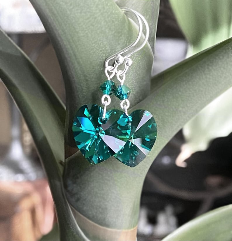 May include: A pair of silver dangle earrings with emerald green heart-shaped crystal accents.