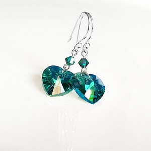 May include: A pair of silver dangle earrings with teal heart-shaped crystal drops.