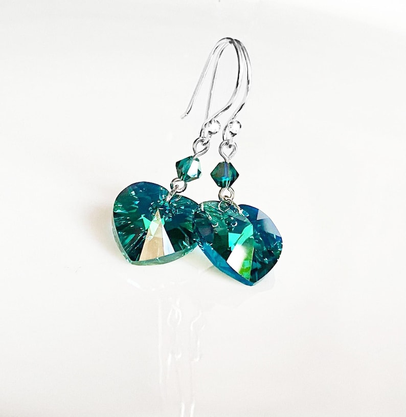 May include: A pair of silver dangle earrings with teal heart-shaped crystal drops.