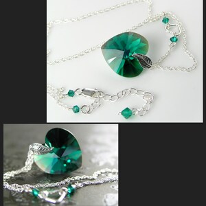 May include: A silver chain necklace with a large emerald green heart-shaped crystal pendant. The pendant has a small silver leaf charm attached to it.