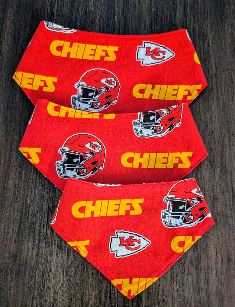 May include: Three red pet bandanas with a repeating pattern of yellow "CHIEFS" text, football helmets, and team logos. The bandanas are arranged in a layered, triangular shape.