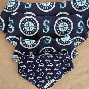Può includere: Bandane per cani blu navy con ancore bianche e loghi dei Seattle Mariners. Le bandane sono di varie dimensioni, con il logo dei Mariners con una rosa dei venti. La bandana più piccola ha un motivo ad ancora bianca.