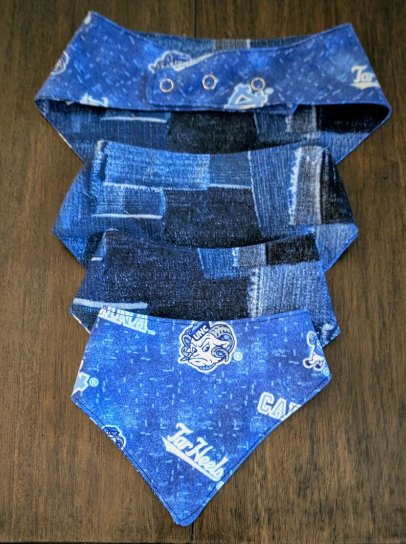 May include: Four blue dog bandanas. The top bandana has a denim pattern with snap closures. The second and third bandanas have a denim patchwork pattern. The bottom bandana has a blue background with the text "Tar Heels" and a ram logo.