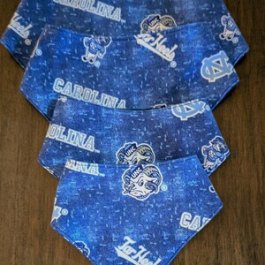 May include: Four blue dog bandanas with a repeating pattern of the words "Carolina", "Tar Heels", and the UNC logo. The bandanas are in various sizes and are made of a soft fabric.