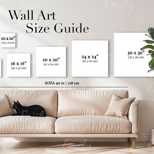 Puede incluir: Una guía de tamaños para arte de pared con diferentes tamaños de impresiones que se muestran en una pared blanca. Los tamaños se enumeran en pulgadas y centímetros. Un sofá está en primer plano con un gato negro acostado sobre él. El texto "SOFA 90 in | 228 cm" está debajo de las impresiones.