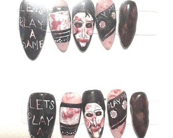 Puede incluir: Un conjunto de diez uñas artificiales con temática de terror. Las uñas están pintadas en negro, rojo y rosa, con los textos "PLAY A GAME" y "LET'S PLAY A GAME". Algunas uñas presentan un diseño de rostro.