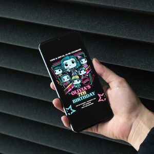 May include: A black smartphone displays a birthday invitation. The invitation features cartoon characters and the text "Olivia's 7th Birthday" in pink and teal. The phone is held against a dark, textured background.