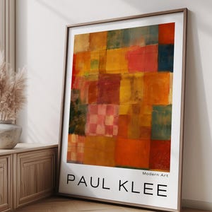 以下が含まれることがあります： 赤、オレンジ、黄色、緑の色合いのカラフルなパッチワークデザインが特徴の、額装された抽象芸術プリント。 プリントには「PAUL KLEE」と「Modern Art」のラベルが付いています。 アートワークは、窓と木の床がある部屋に展示されています。