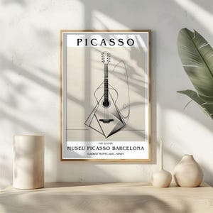 Puede incluir: Impresi&oacute;n art&iacute;stica enmarcada con una ilustraci&oacute;n en blanco y negro de una guitarra cubista. La impresi&oacute;n incluye el nombre "PICASSO" en la parte superior y el texto "THE GUITAR MUSEU PICASSO BARCELONA CARRER MONTCADA - SPAIN" en la parte inferior.