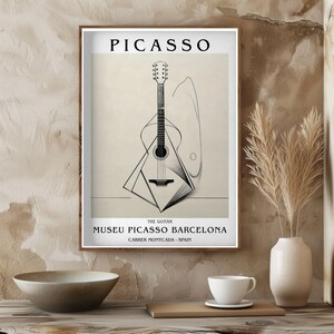 Puede incluir: Una impresi&oacute;n art&iacute;stica enmarcada con una ilustraci&oacute;n abstracta en blanco y negro de una guitarra. La impresi&oacute;n incluye el nombre "PICASSO" en la parte superior y el texto "THE GUITAR MUSEU PICASSO BARCELONA CARRER MONTCADA - SPAIN" en la parte inferior.