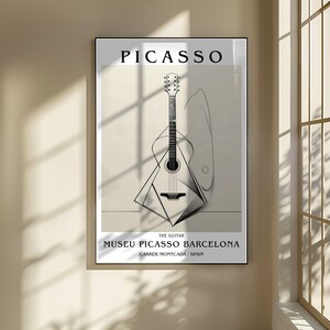 Puede incluir: Impresi&oacute;n art&iacute;stica enmarcada con una ilustraci&oacute;n en blanco y negro de una guitarra, con la palabra "PICASSO" en la parte superior. El texto "MUSEU PICASSO BARCELONA" y "CARRER MONTCADA - SPAIN" est&aacute;n debajo. La obra se exhibe en una pared beige.