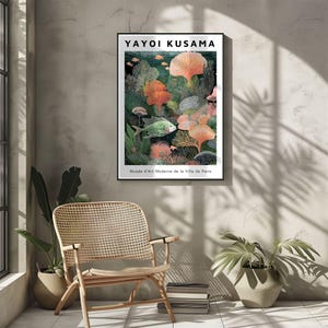 May include: A framed art print featuring a vibrant underwater scene with coral, fish, and plant life in shades of green, orange, and pink. The print is by Yayoi Kusama and is displayed in a room with a woven chair and potted plants.