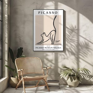 Puede incluir: Un cuadro enmarcado con un dibujo lineal minimalista de un gato estir&aacute;ndose. El cuadro tiene la palabra "PICASSO" en la parte superior y "PICASSO MUSEUM M&Aacute;LAGA" en la parte inferior. El fondo es de color beige neutro.