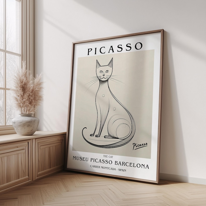 May include: A framed art print featuring a stylized black and white illustration of a cat, with the name "Picasso" at the top. The print includes text for the Museu Picasso Barcelona.