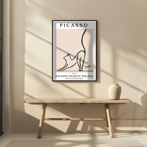 Puede incluir: Un cuadro enmarcado con un dibujo lineal negro de un gato estir&aacute;ndose. El cuadro incluye el nombre "PICASSO" en la parte superior y "PICASSO MUSEUM M&Aacute;LAGA" en la inferior, sobre un fondo beige claro.
